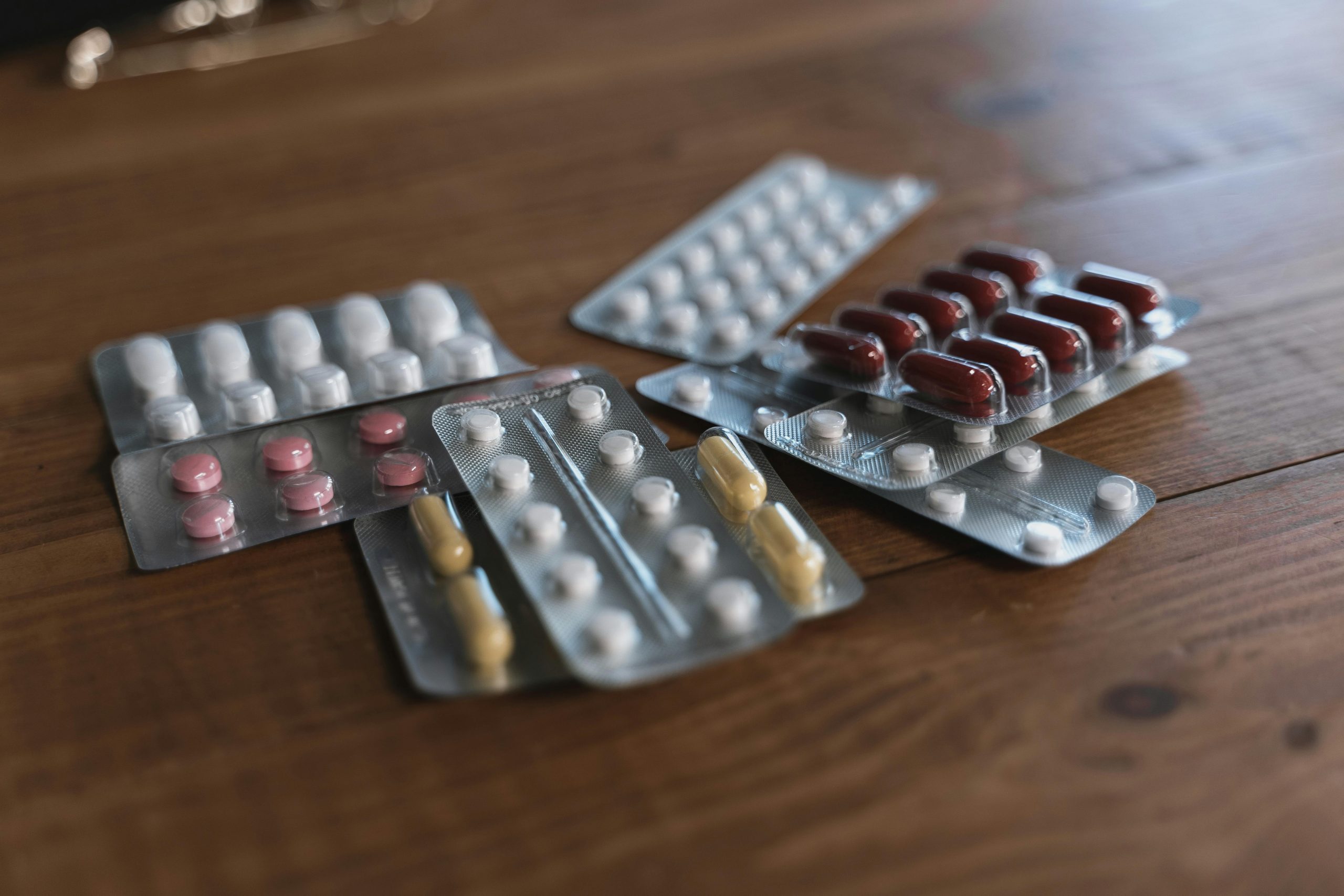 A variety of pills in blister packs displayed on a wooden surface. Ideal for health-related content.